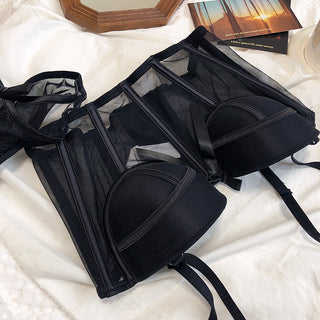 Flat lay of the Shannon bra and pantie set in black on a white sheet with accessories in the background